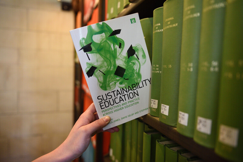 A hand removing a book from a library shelf, the book is titled sustainability education